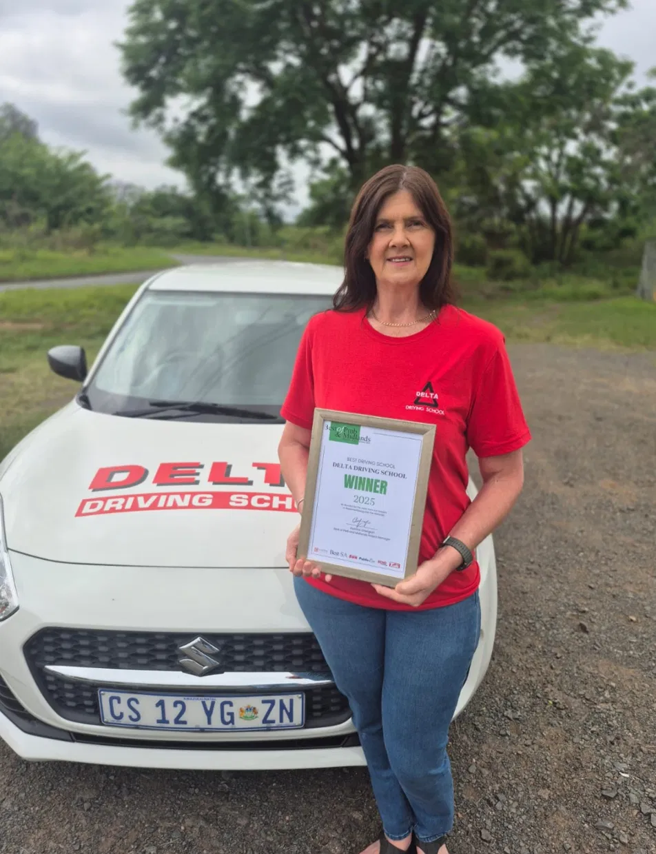 Linda, owner of Delta Driving School, holding the 2025 Best of PMB & Midlands Best Driving School winner award in front of the Delta Driving School branded car
